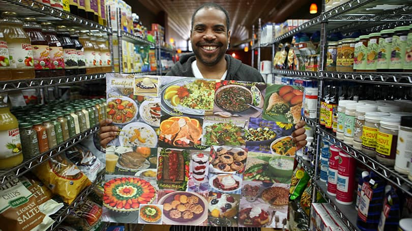 Man in grocery store holding up a poster of food